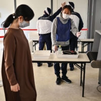 Volunteers for the Olympic Games practice screening measures in Tokyo on Oct. 21.   | AFP-JIJI