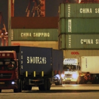 Trucks transport shipping containers at a dockyard in Qingdao in east China\'s Shandong province last month.  | CHINATOPIX / VIA AP
