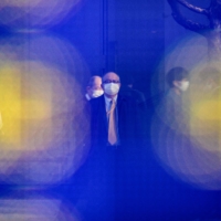 Mask-wearing pedestrians are reflected in a board in Tokyo. | AFP-JIJI