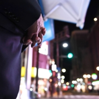 A man in his 60s, who started as a bouncer in his early 30s and now works for an exclusive club, stands on the corner of an intersection in the Nakasu district of Fukuoka in October. | NISHINIPPON SHIMBUN


