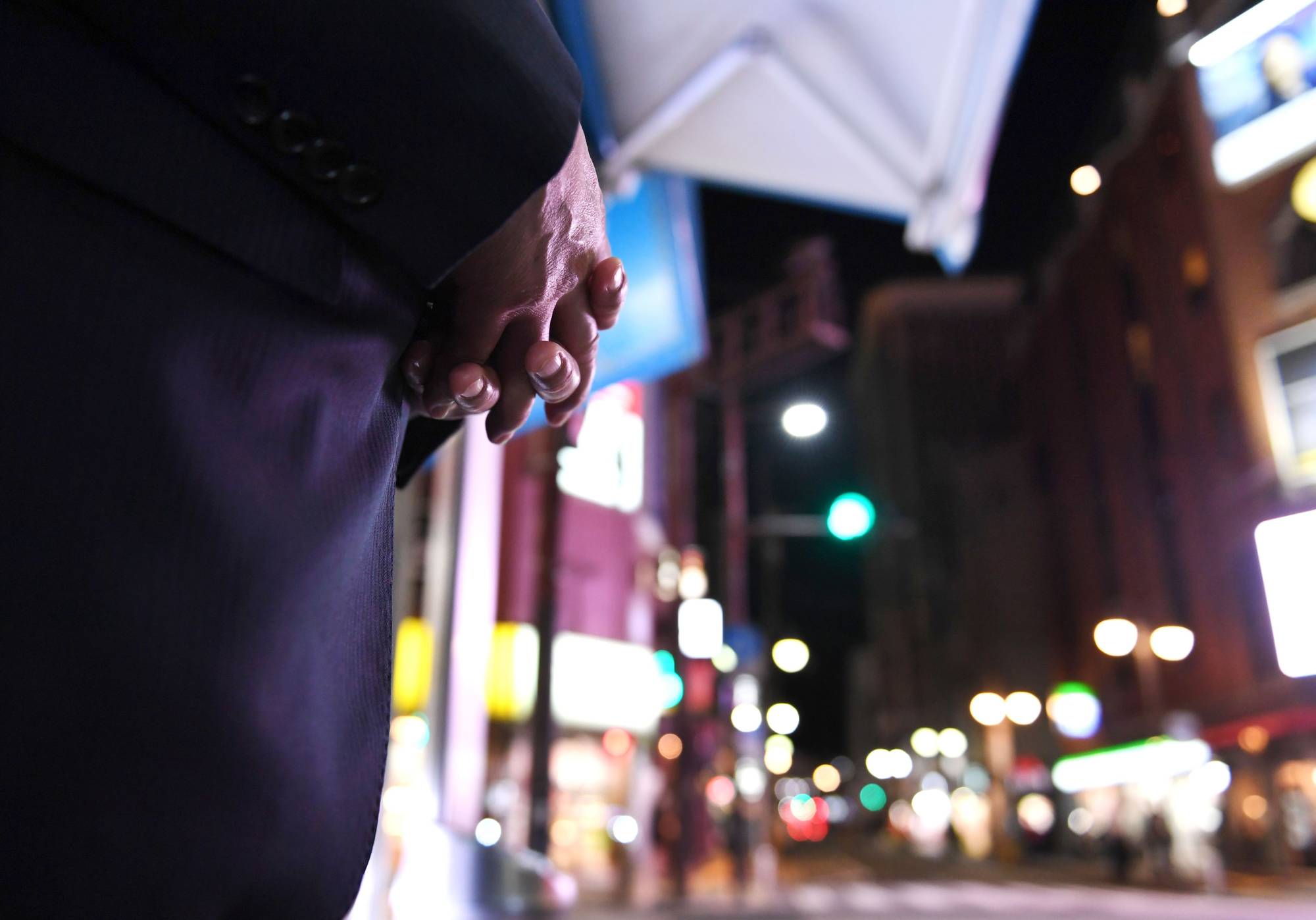 A man in his 60s, who started as a bouncer in his early 30s and now works for an exclusive club, stands on the corner of an intersection in the Nakasu district of Fukuoka in October. | NISHINIPPON SHIMBUN 