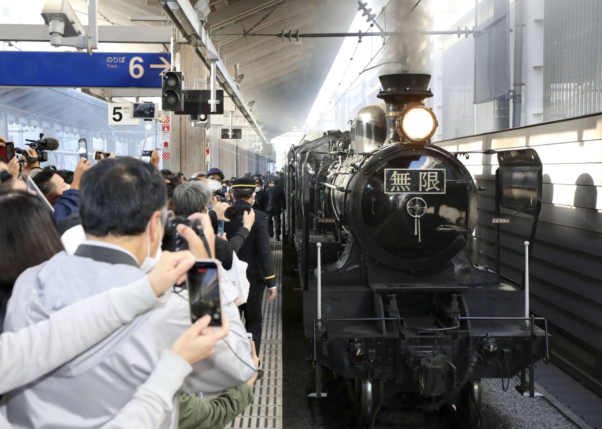 People take photos of a special train with livery in the style of the movie of the popular 'Demon Slayer' ('Kimetsu no Yaiba') manga series at Kumamoto Station on Sunday. | KYODO