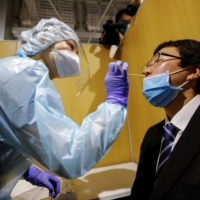 A medical worker wearing a protective suit conducts a simulation for a polymerase chain reaction (PCR) test at the newly opened Narita International Airport PCR Center on Monday. | REUTERS