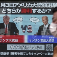 A man walks past a screen showing illustrations depicting Republican President Donald Trump and Democratic candidate and former Vice President Joe Biden for an online vote to predict the winner in the U.S. presidential election, in Tokyo on Oct. 26. | AP
