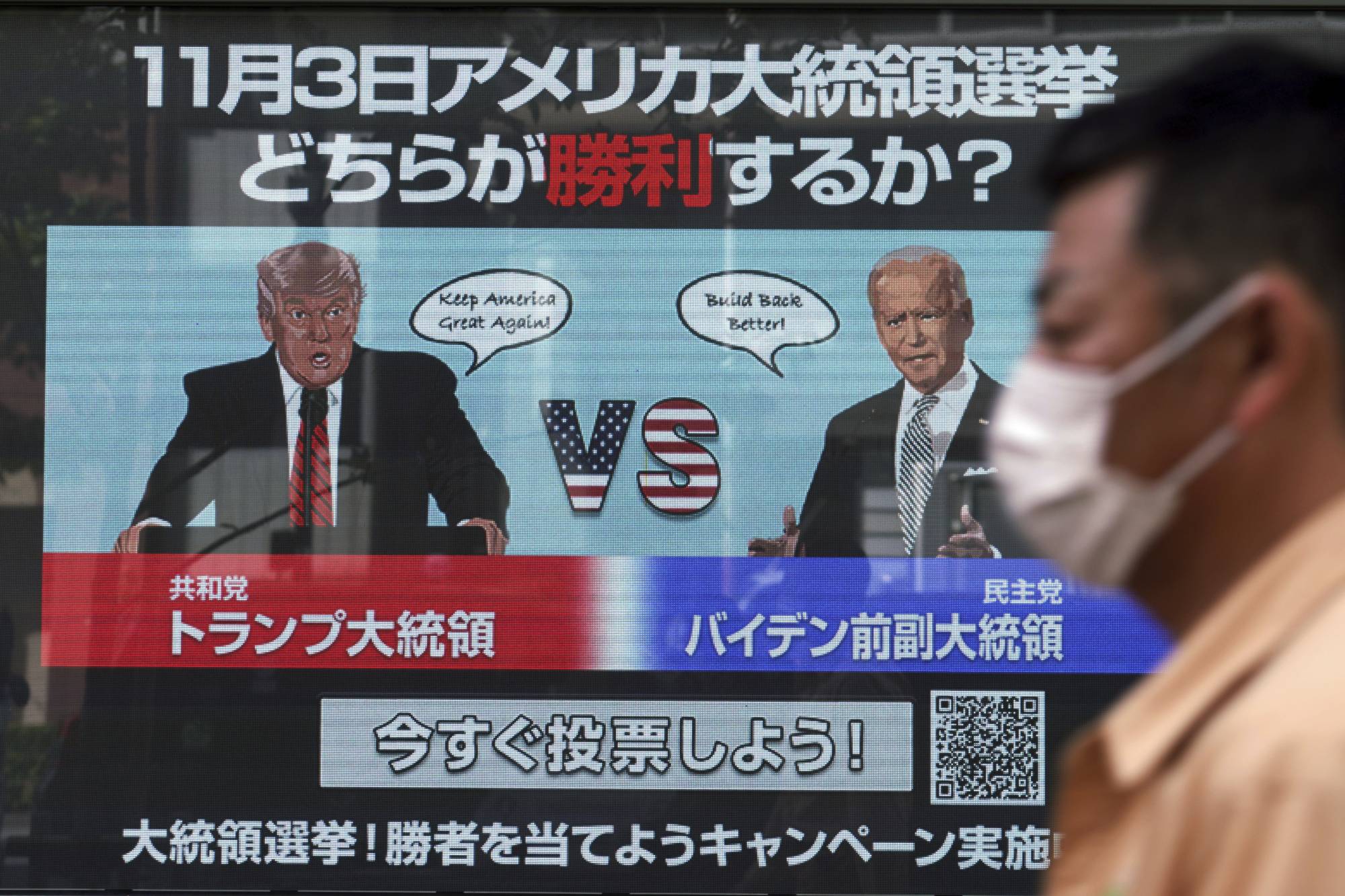 A man walks past a screen showing illustrations depicting Republican President Donald Trump and Democratic candidate and former Vice President Joe Biden for an online vote to predict the winner in the U.S. presidential election, in Tokyo on Oct. 26. | AP