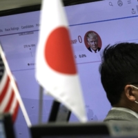 A money trader of a foreign exchange company works near a screen showing a news program on the U.S. elections on Wednesday in Tokyo. | AP