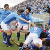 Yokohama FC players including Kazuyoshi Miura (second from left) pile on Reo Yasunaga after he scores the game-winning goal on Sunday in Yokohama. | KYODO