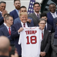 President Donald Trump holds a Red Sox team jersey presented by outfielder and designated hitter J.D. Martinez (right) during a Rose Garden ceremony outside the White House on May 9, 2019, in Washington. | REUTERS