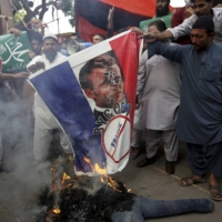 Supporters of Jamaat-e-Islami, a religious political party, burn a representation of a French flag with a defaced image of French President Emmanuel Macron during a protest in Karachi, Pakistan, on Friday. | AP