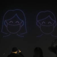 Over 300 drones fly in the shape of people wearing face masks over Olympic Park in Seoul on Friday. | AP