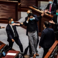 Pro-democracy legislator Ted Hui is removed by security guards after throwing a jar containing a foul-smelling liquid onto the floor during a June Legislative Council debate on a law that bans insulting China\'s national anthem.  | AFP-JIJI