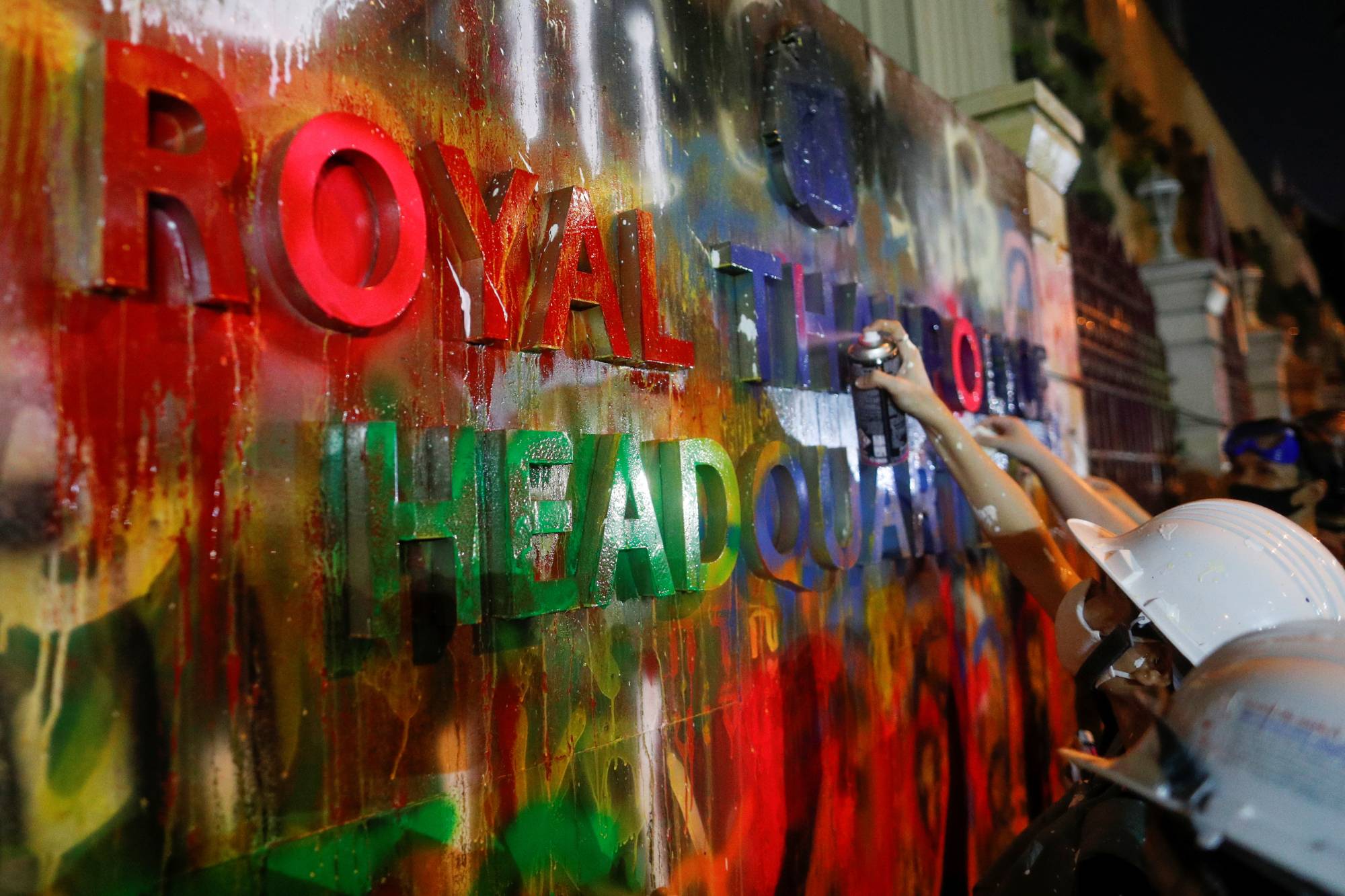 Demonstrators spray-paint a plaque in front of the police headquarters during a rally in Bangkok on Wednesday. | Reuters 