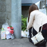 A woman lays flowers in front of the apartment building in Sapporo where two-year-old Kotori Ikeda died in June 2019. | KYODO
