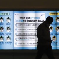 A man wearing a face mask walks past in front of a screen showing precautions against the coronavirus in Seoul on Friday. The letters read: \"How to wear a mask.\"  | AP