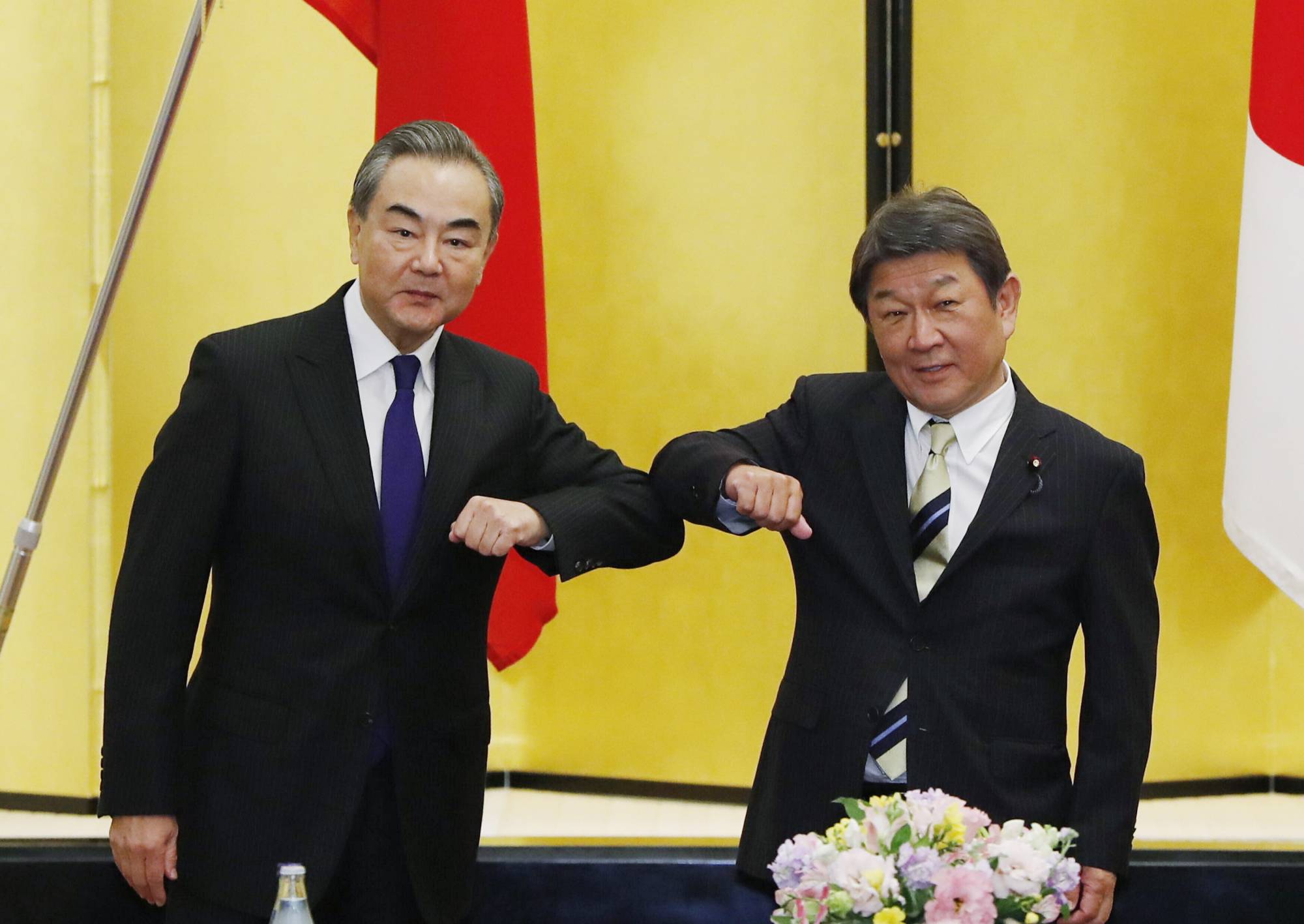 Chinese Foreign Minister Wang Yi (left) and his Japanese counterpart, Toshimitsu Motegi, bump elbows as they meet in Tokyo on Tuesday. | POOL / VIA AP