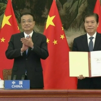Chinese Premier Li Keqiang (left) applauds on Nov. 15 as China’s minister of commerce, Zhong Shan, holds up an agreement during the signing ceremony for the Regional Comprehensive Economic Partnership trade pact during the online ASEAN summit.  | VIETNAM HOST BROADCASTER / VIA AFP-JIJI