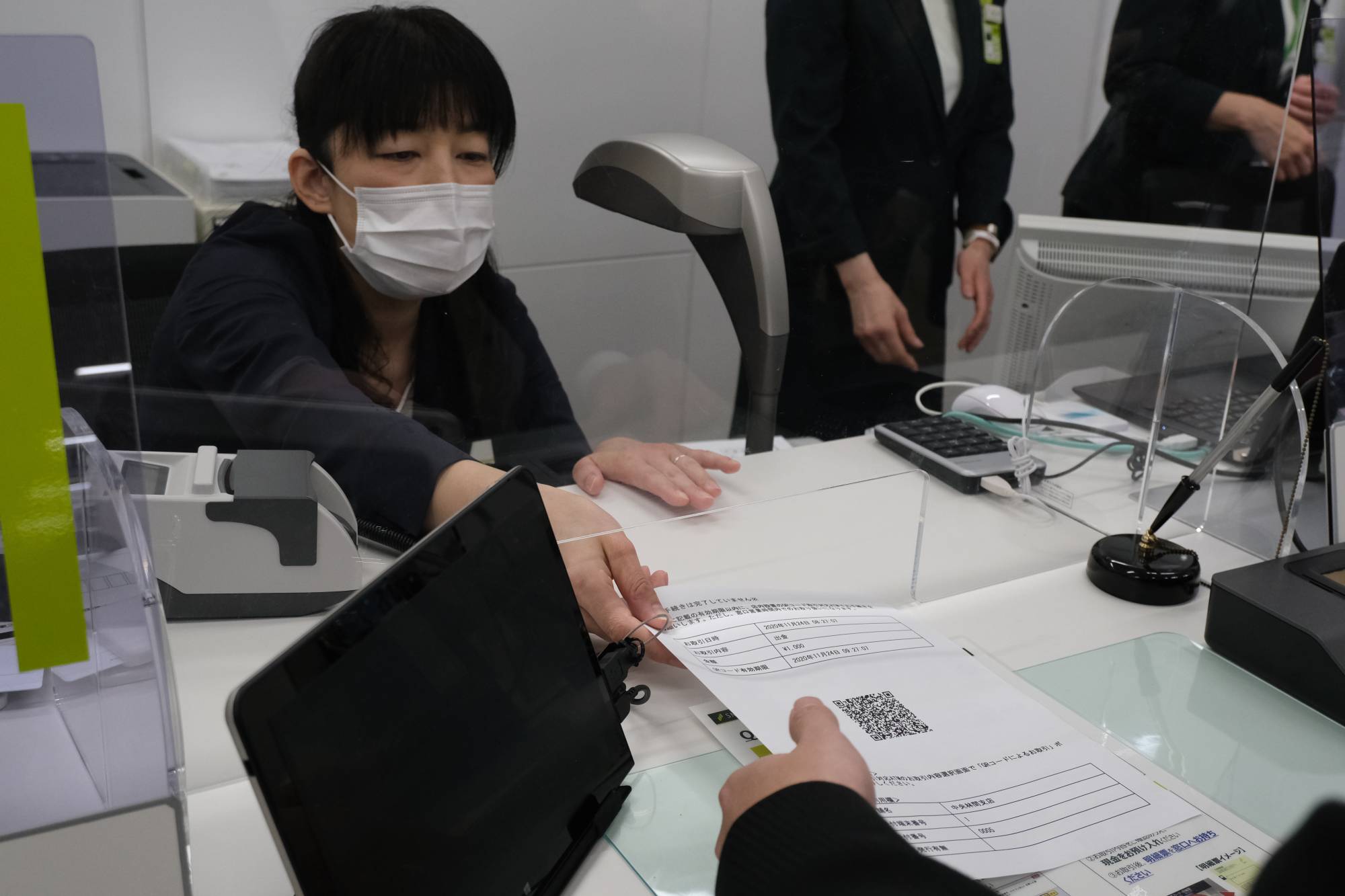 A Sumitomo Mitsui Bank employee hands out a paper slip with a QR code that will allow a customer to withdraw cash at the ATM, on Tuesday at its Chuorinkan branch in Yamato, Kanagawa Prefecture. | KAZUAKI NAGATA