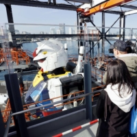 Reporters look at the side of a life-size statue of Gundam set up at Yokohama Pier on Monday. | KYODO