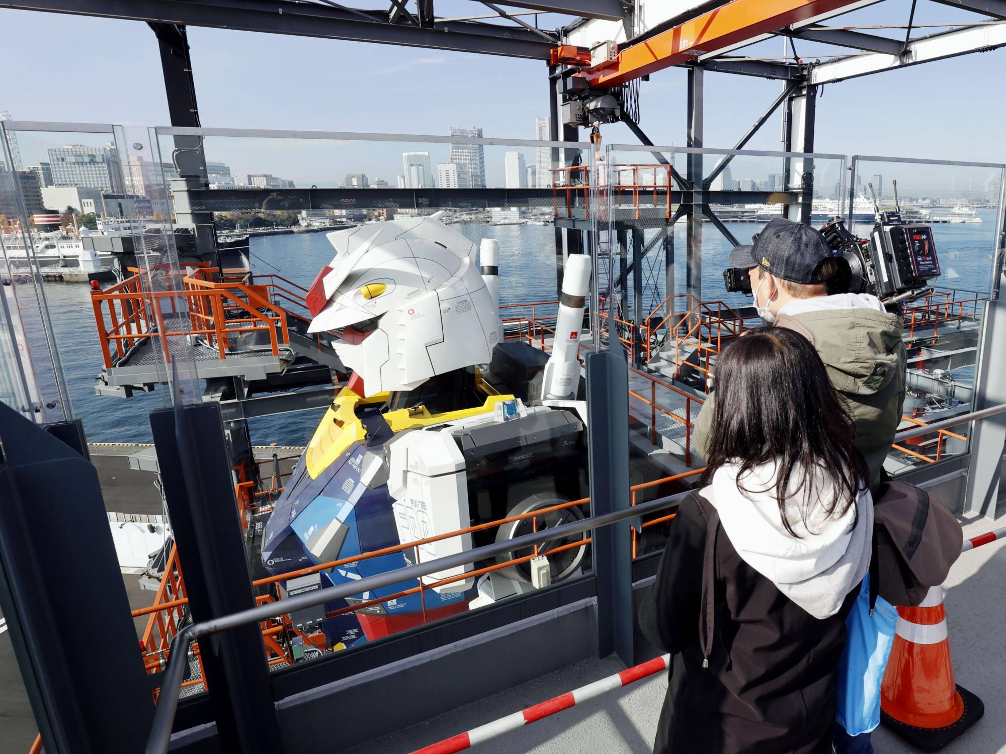 Reporters look at the side of a life-size statue of Gundam set up at Yokohama Pier on Monday. | KYODO