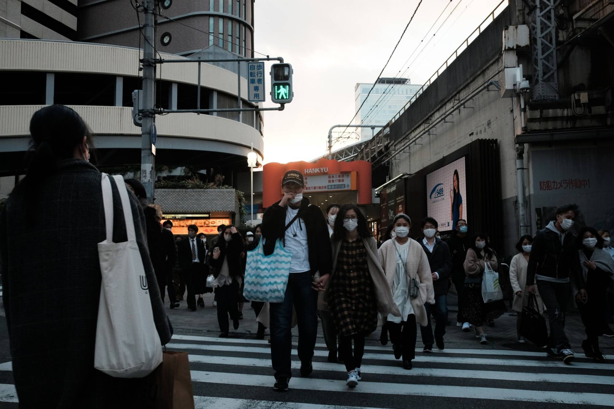 Pedestrians cross a road in front of Osaka Station on Sunday. Tokyo and Osaka last week called on some businesses to close early, while Hokkaido implemented its own measures to stem the virus’s spread. | BLOOMBERG