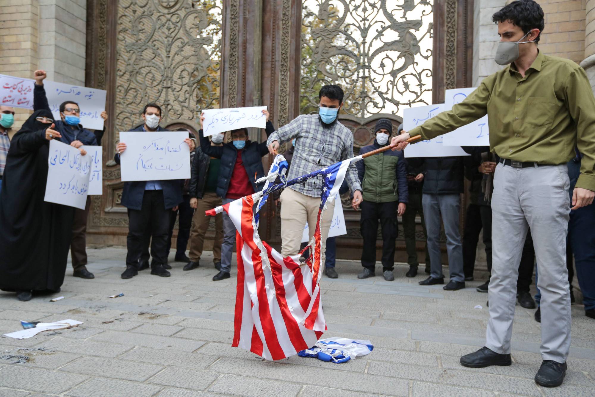 Students of Iran's Basij paramilitary force burn U.S. and Israeli flags in front of the foreign ministry in Tehran on Saturday to protest the killing of prominent nuclear scientist Mohsen Fakhrizadeh. | AFP-JIJI  