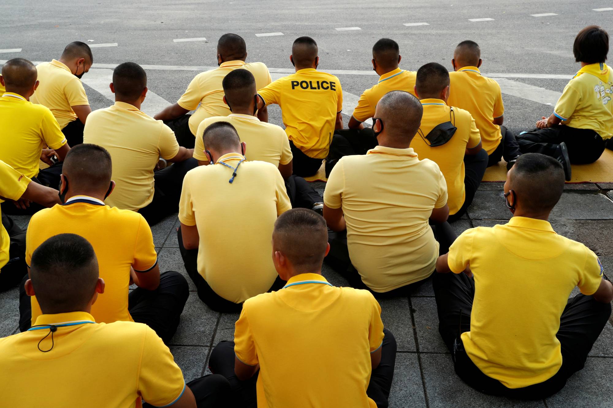 Police officers sit on the ground after the motorcade carrying Thailand's King Maha Vajiralongkorn and Queen Suthida drove past in Bangkok in October. | REUTERS