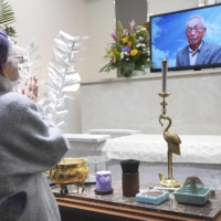 Tamae Menda, widow of Sakae Menda, prays in front of a display showing her husband, in Omuta, Fukuoka Prefecture, on Saturday. | KYODO