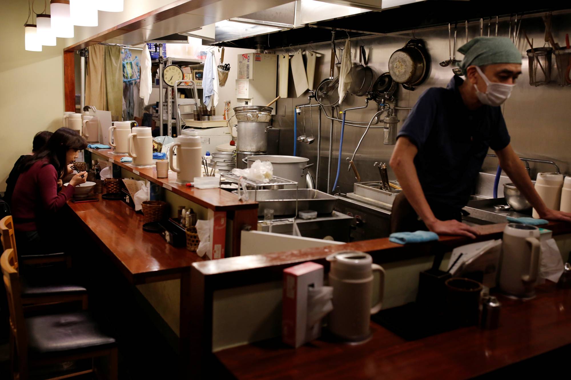 Yashiro Haga, owner of the Shirohachi ramen shop, waits for his last customers to finish their bowls on Thursday, his final day of business. | REUTERS
