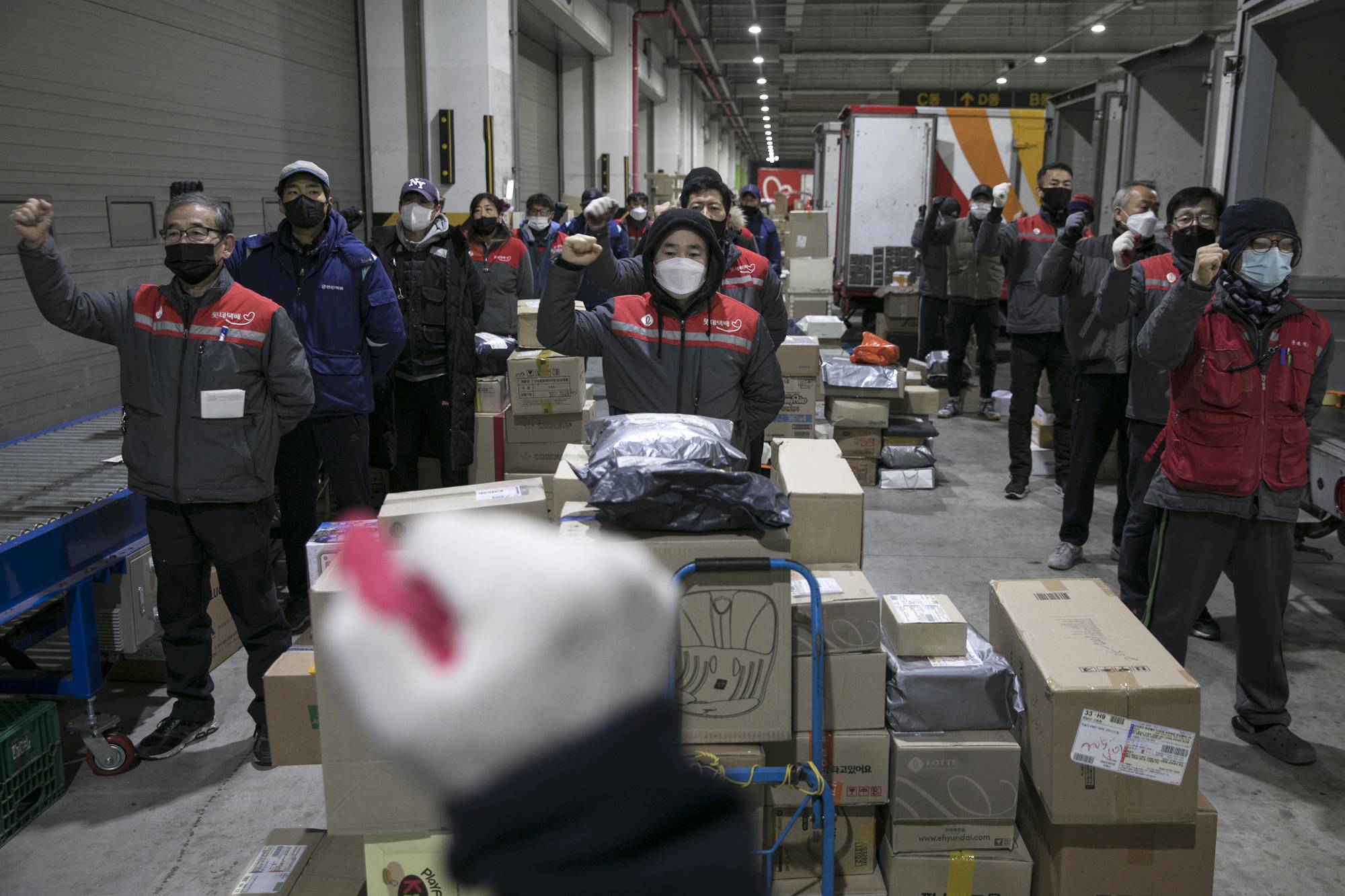 Couriers raise their fists while singing a union song at a depot in Seoul. More than a dozen couriers have died this year, some after complaining of unbearable workloads that kept them on the clock from dawn until past midnight. | Woohae Cho / The New York Times