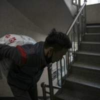 Park Ki-Ryeon hauls a bag of rice up flights of stairs during a delivery last month near Seoul.  | WOOHAE CHO / THE NEW YORK TIMES