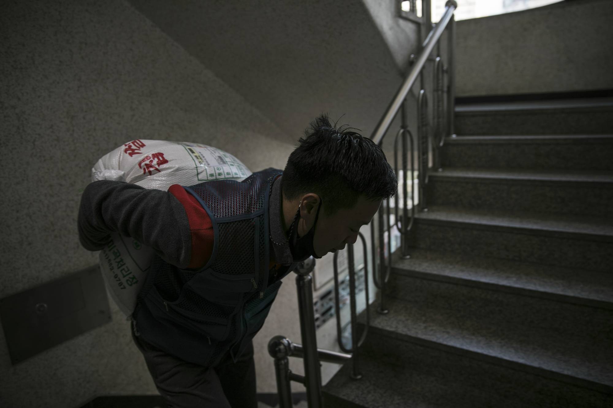 Park Ki-Ryeon hauls a bag of rice up flights of stairs during a delivery last month near Seoul. | Woohae Cho / The New York Times