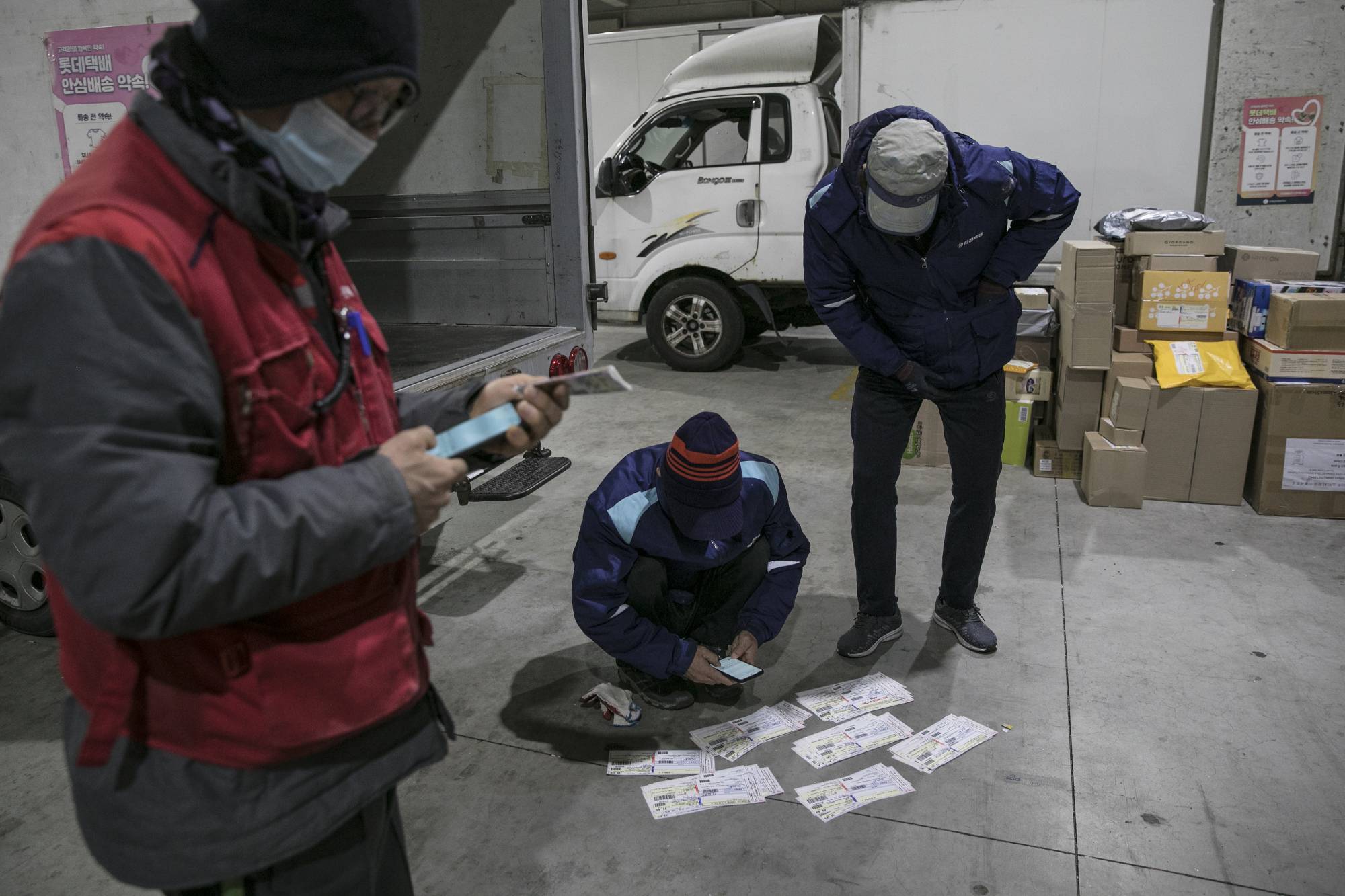 Couriers check delivery addresses at a distribution center in Seoul on Nov. 30. | Woohae Cho / The New York Times