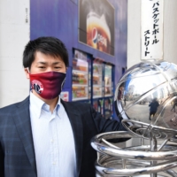 Ryo Shinkawa, a member of the Wizards\' Japanese-language media team, poses with a statue at the entrance of Shibuya\'s Basketball Street on Nov. 18. | DAN ORLOWITZ

