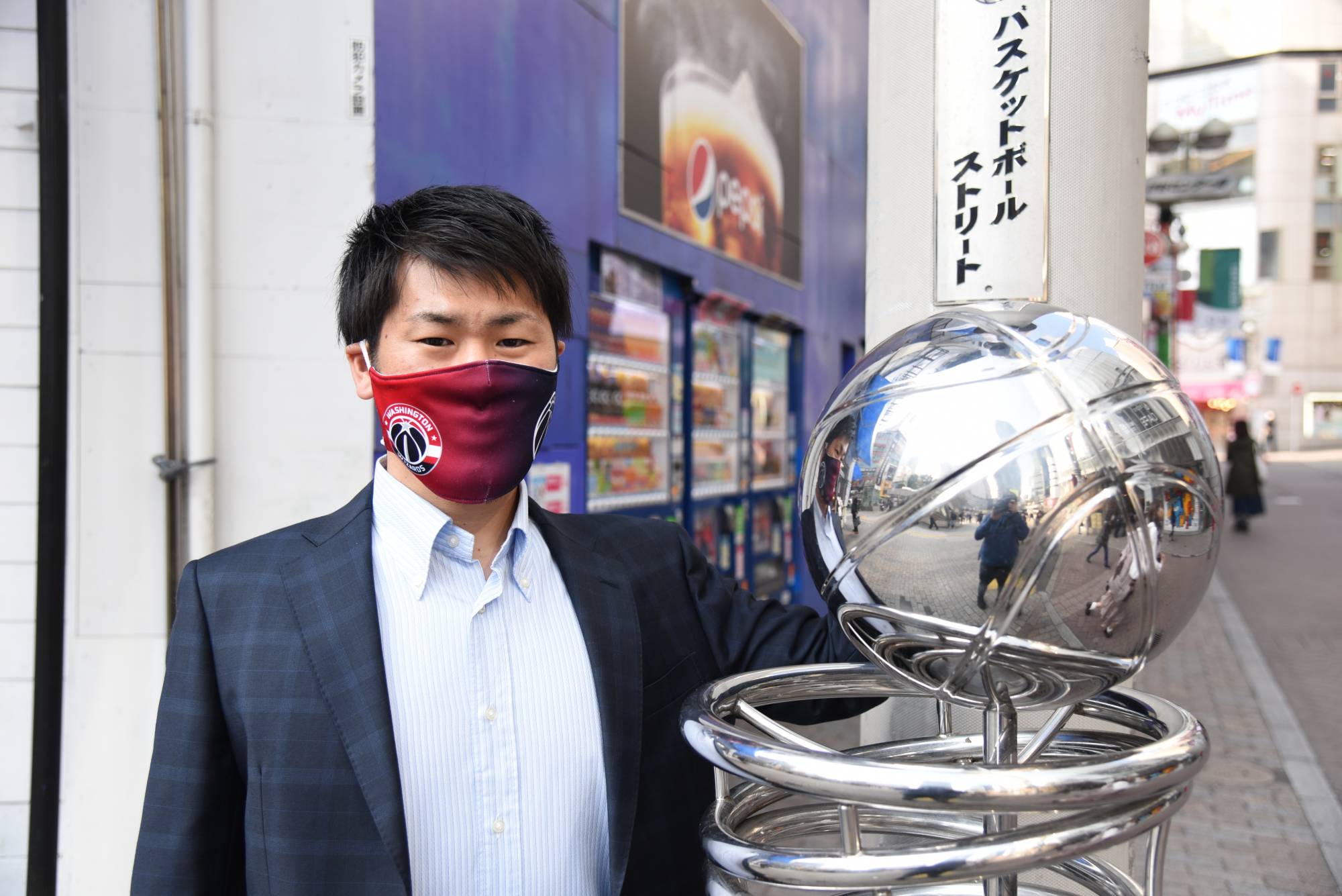 Ryo Shinkawa, a member of the Wizards' Japanese-language media team, poses with a statue at the entrance of Shibuya's Basketball Street on Nov. 18. | DAN ORLOWITZ 