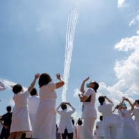 Medical workers watch the Blue Impulse aerobatic team of the Air Self-Defense Force as they fly over a hospital to salute the medical workers at the front line of the fight against COVID-19 in Tokyo on May 29. | REUTERS
