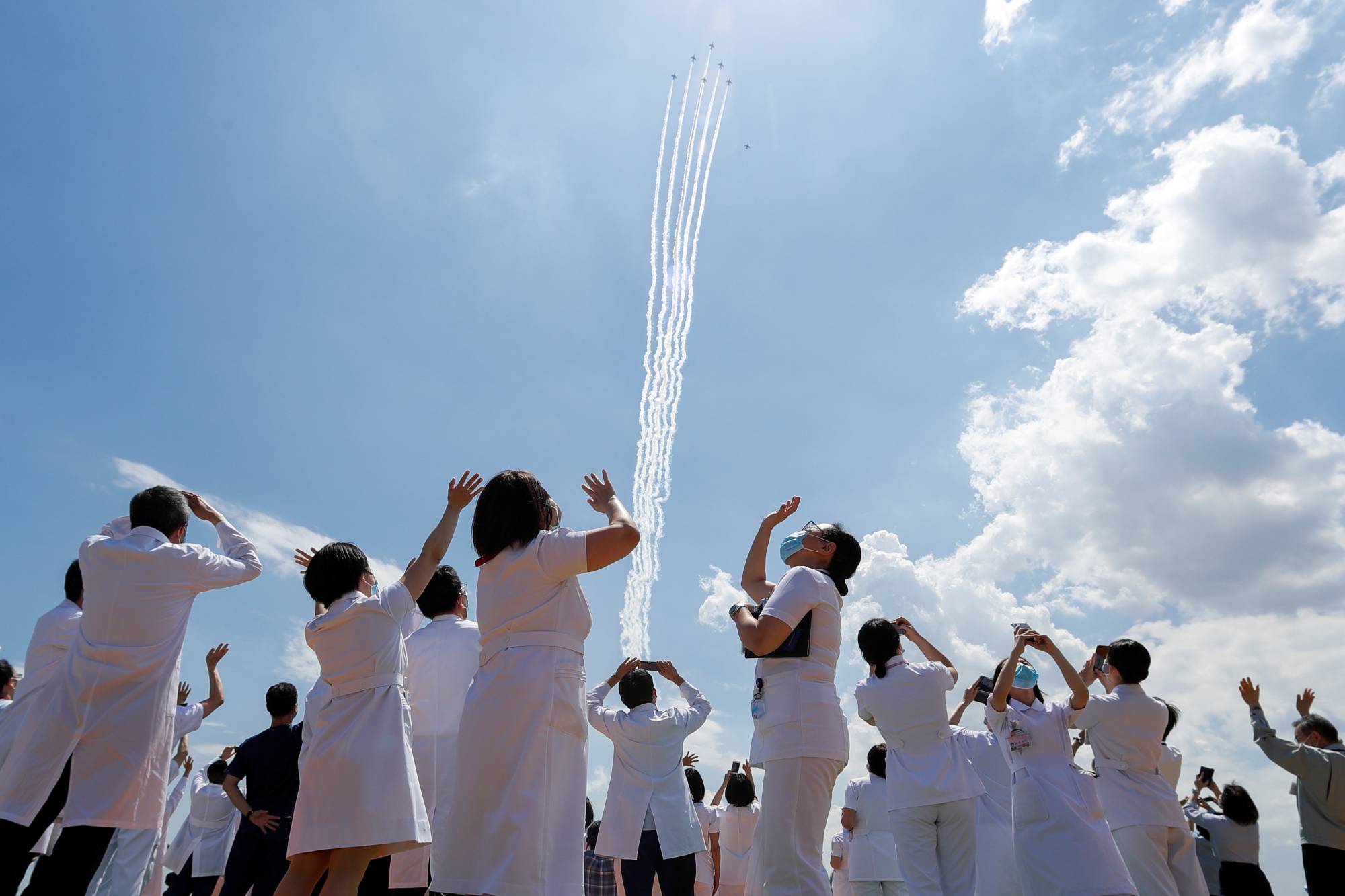 Medical workers watch the Blue Impulse aerobatic team of the Air Self-Defense Force as they fly over a hospital to salute the medical workers at the front line of the fight against COVID-19 in Tokyo on May 29. | REUTERS