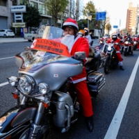 People dressed in Santa Claus costumes ride their motorbikes during the Xmas Toy Run parade to rev up the holiday spirit and rally against child abuse in Tokyo on Sunday. | REUTERS