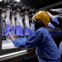 A worker inspects gloves at the Top Glove factory in Shah Alam, Malaysia, in August.  | REUTERS 