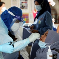 A medical worker collects a swab sample from a Top Glove worker in Klang, Malaysia, in November.  | REUTERS 