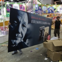 Workers carry an advertisement promoting the Chinese edition of \"Deng Xiaoping and the Transformation of China\", written by Harvard University Professor Emeritus Ezra Vogel, during a media preview of the Hong Kong Book Fair in 2013. | REUTERS 