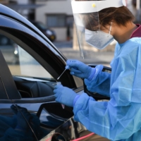 A health care worker collects a swab sample at the drive-thru coronavirus testing center set up at Fujimino Emergency Hospital in Miyoshi, Saitama Prefecture, Japan, earlier this month. | BLOOMBERG