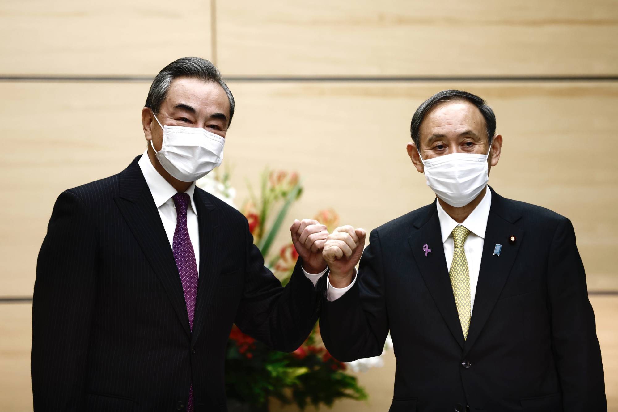 Wang Yi (left), China's foreign minister, bumps elbows with Prime Minister Yoshihide Suga ahead of their meeting in Tokyo on Nov. 25. | AFP-JIJI