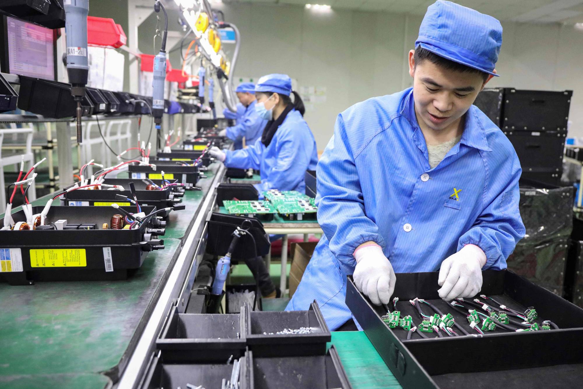 Employees work on photovoltaic products at a renewable energy company in Tonglu, China, on Wednesday. China will overtake the United States to become the world's biggest economy in 2028, five years earlier than previously estimated due to the contrasting recoveries of the two countries from the COVID-19 pandemic, a think tank said. | AFP-JIJI