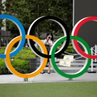 A woman wearing a protective mask takes a picture of the Olympic rings in front of the National Stadium in Tokyo on Oct. 14. | REUTERS