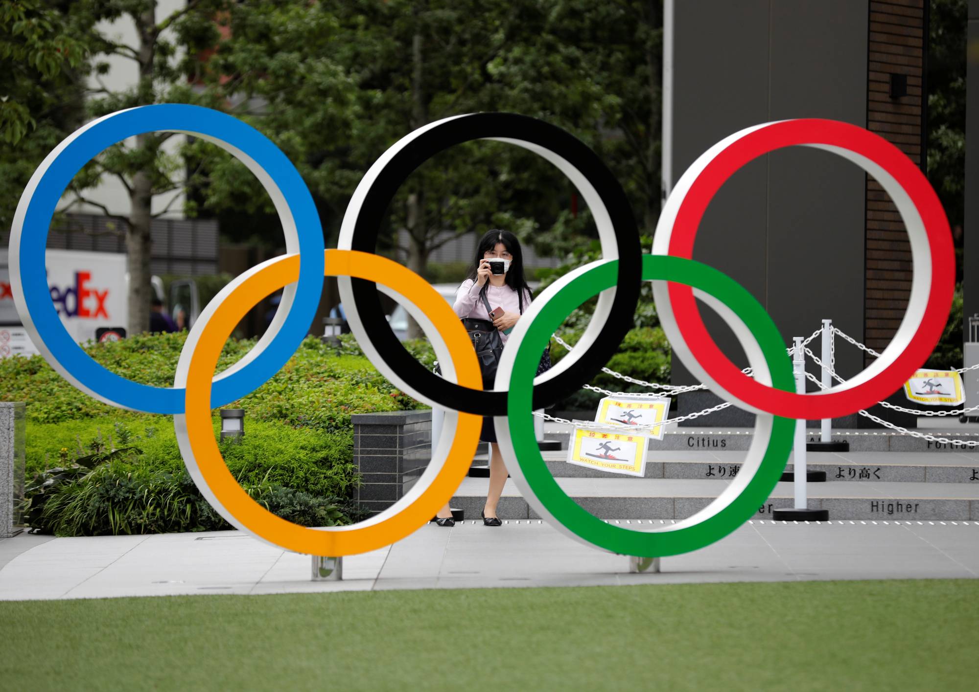 A woman wearing a protective mask takes a picture of the Olympic rings in front of the National Stadium in Tokyo on Oct. 14. | REUTERS