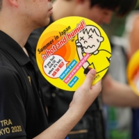 Visitors use paper fans featuring attention-seeking messages about heat during a test of heat countermeasures for the Tokyo 2020 Olympic and Paralympic Games during a FIVB Beach Volleyball World Tour event  on July 25, 2019. | REUTERS
