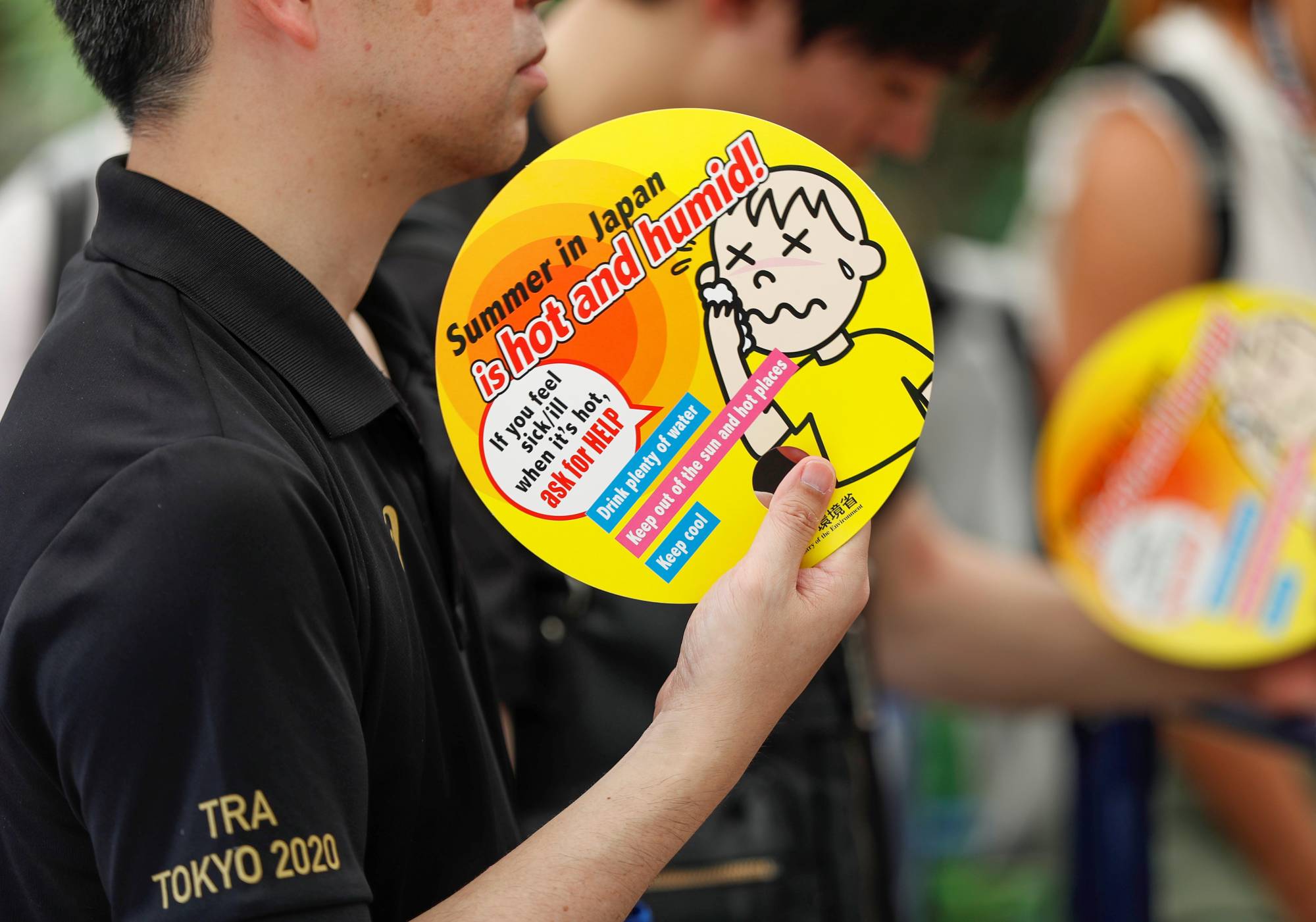Visitors use paper fans featuring attention-seeking messages about heat during a test of heat countermeasures for the Tokyo 2020 Olympic and Paralympic Games during a FIVB Beach Volleyball World Tour event  on July 25, 2019. | REUTERS