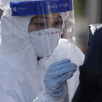 A medical worker takes samples from a woman at a COVID-19 testing site in Seoul on Dec. 12. | AP