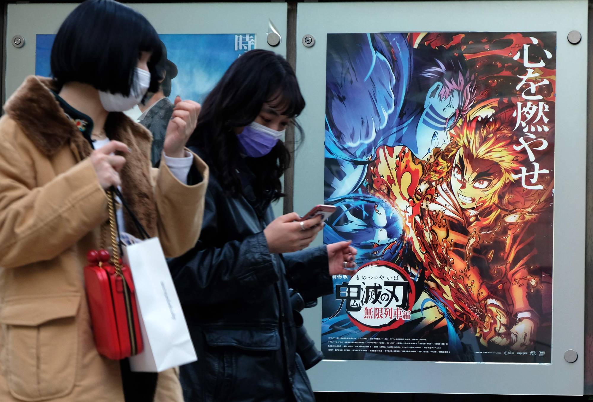 Pedestrians walk past a poster promoting the anime film 'Demon Slayer: Kimetsu no Yaiba the Movie: Mugen Train' at a cinema in Tokyo on Dec. 16. The movie became the highest-grossing film in Japanese box-office history on Monday. | AFP-JIJI