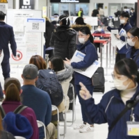 Travelers arriving from overseas wait in line for quarantine at Narita International Airport on Sunday. | KYODO